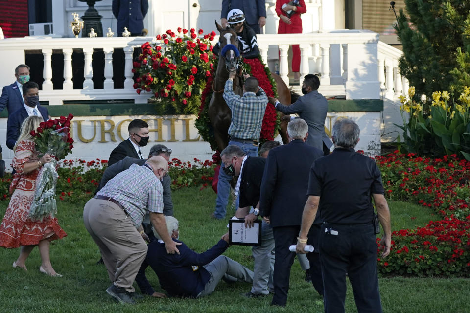 FILE - In this Sept. 5, 2020, file photo, trainer Bob Baffert is helped to get up after being knocked to the ground by his winning horse Authentic ridden by Jockey John Velazquez in the winners' circle after winning the 146th running of the Kentucky Derby at Churchill Downs in Louisville, Ky. Baffert is undefeated taking the Kentucky Derby winner to the Preakness, but for the first time in 20 years he’ll do so without assistant trainer Jimmy Barnes, who broke his right wrist in a paddock accident at Churchill Downs. (AP Photo/Jeff Roberson, File)