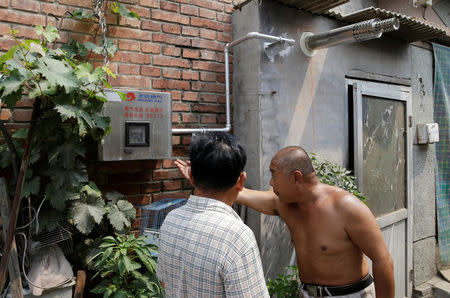 Yao Guanghui (R) explains to his neighbor next to a gas meter connected with the boiler for heating in winter outside his house in Xiaozhangwan village of Tongzhou district, on the outskirts of Beijing, China June 28, 2017. Picture taken June 28, 2017. REUTERS/Jason Lee