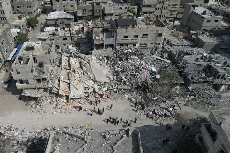 Palestinos junto al edificio destruido en un ataque aéreo israelí en el campamento de Nuseirat, en el centro de la Franja de Gaza, el lunes 16 de octubre de 2023. (AP Photo/Hatem Moussa)