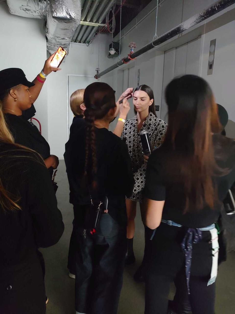 A model is surrounded by a group of people touching up her hair and makeup