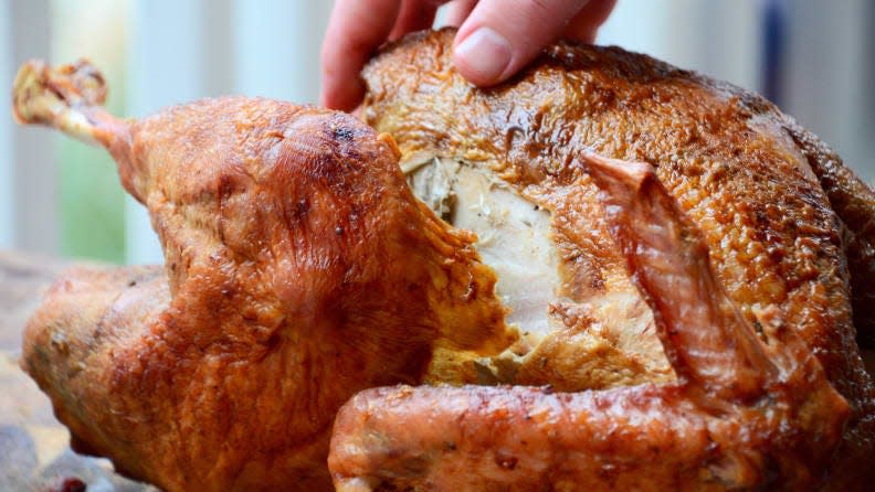 A hand touching a cooked turkey, viewed from the side.