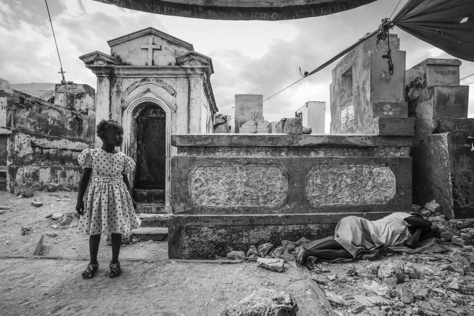 On the fifth anniversary of the devastating earthquake, a young child stands to the side of her mourning mother who lies weeping nearby in the Grand Cemetery of Port-Au-Prince, Haiti, Jan. 12, 2015.