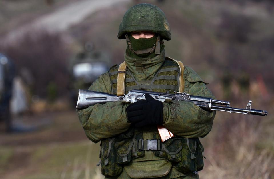 A soldier wearing a face mask and large helmet and carrying a rifle.