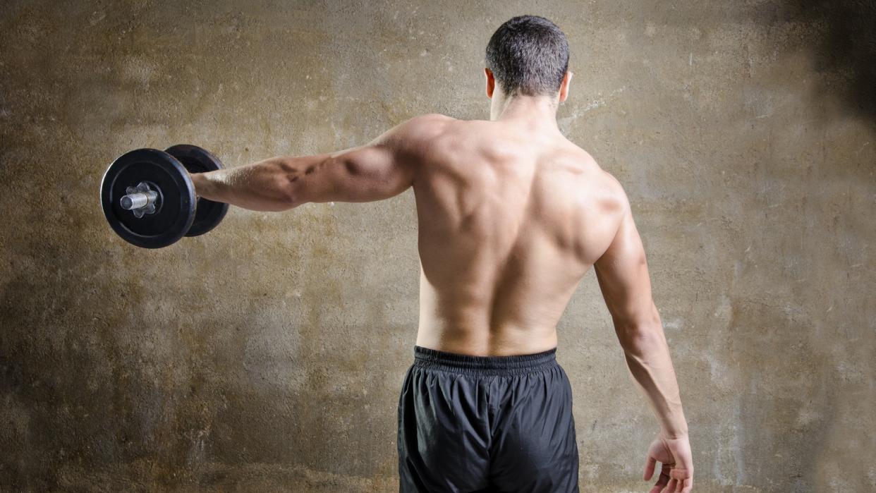  Man with back to camera performing single-arm dumbbell lateral raise left arm. 