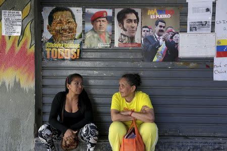 Women talk while seated under images of Venezuela's late President Hugo Chavez, national hero Simon Bolivar (2nd R) and Venezuela's current President Nicolas Maduro (R), close to the National Assembly building that was in session in Caracas December 22, 2015. REUTERS/Marco Bello