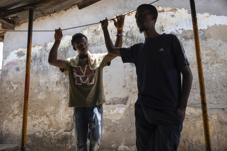 Allassane Sylla, left, and Ousmane Holia Diallo, brother and cousin of the late Ousmane Sylla, talk under a shade before the return of Sylla's body in Conakry, Guinea, Monday, April 8, 2024. (AP Photo/Misper Apawu)