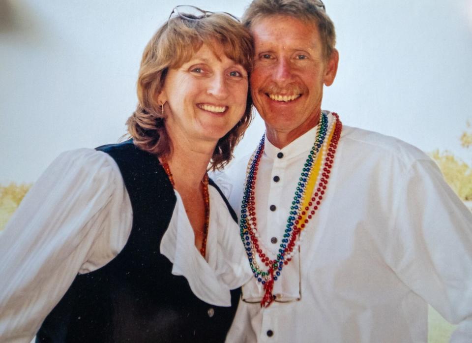 A woman at left and a man at right press their heads together as they smile wide while posing for the camera.