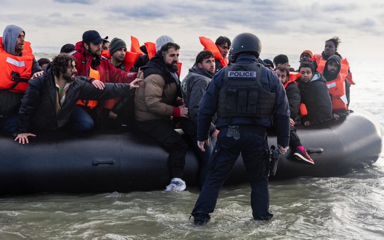 A French police officer confronts migrants in a dinghy as they attempt to depart Gravelines, near Dunkirk, on Friday
