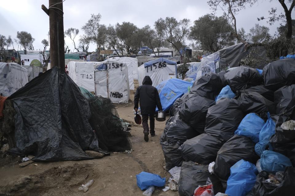 A migrant walks in front of garbage bags dumped outside the Moria refugee camp on the northeastern Aegean island of Lesbos, Greece, on Tuesday, Jan. 21, 2020. Some businesses and public services on the eastern Aegean island are holding a 24-hour strike on Wednesday to protest the migration situation, with thousands of migrants and refugees are stranded in overcrowded camps in increasingly precarious conditions.(AP Photo/Aggelos Barai)