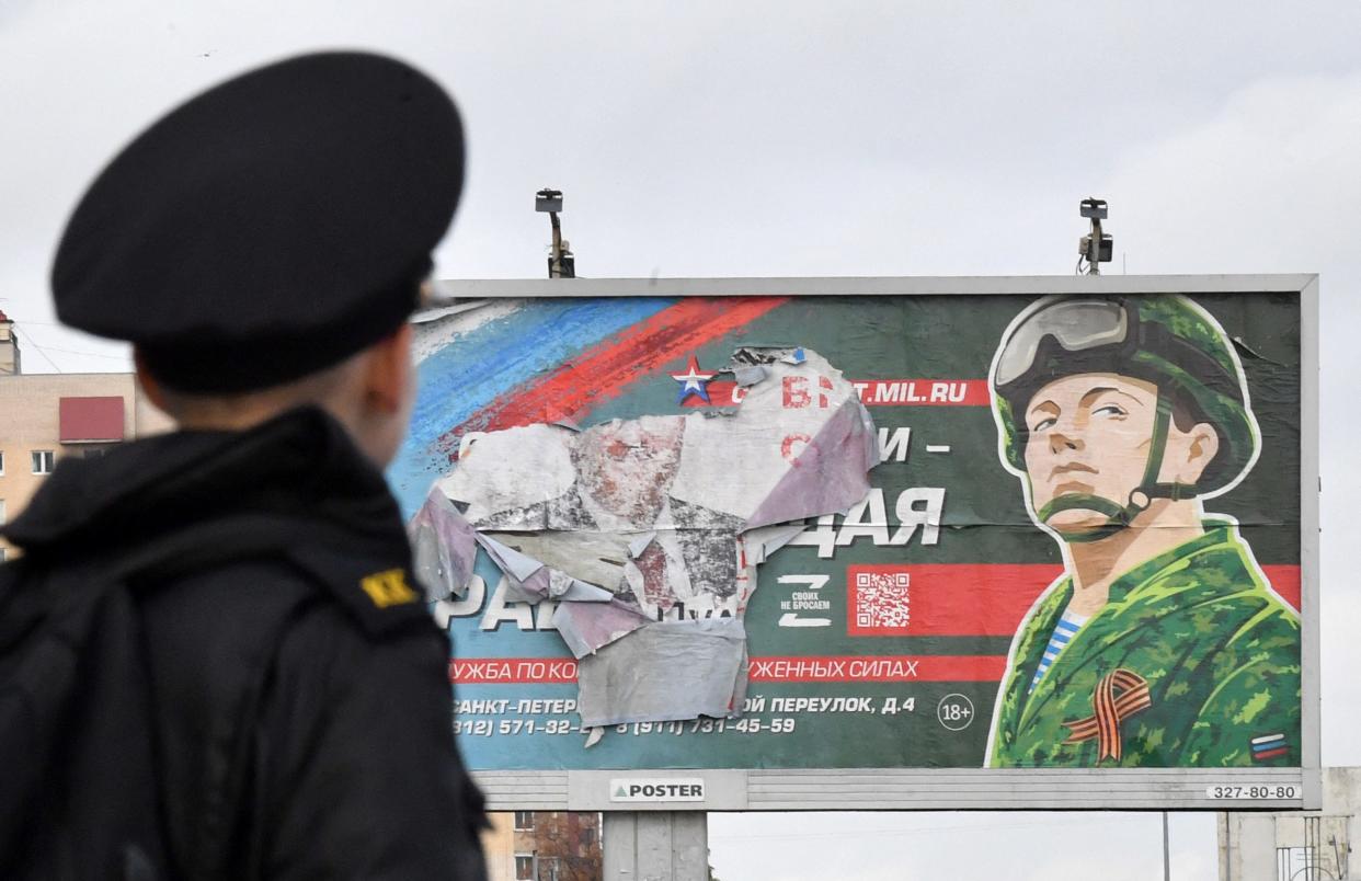 A military cadet stands in front of a billboard promoting contract army service in Saint Petersburg on October 5, 2022. - Russian President Vladimir Putin announced on September 21 a mobilisation of hundreds of thousands of Russian men to bolster Moscow's army in Ukraine, sparking demonstrations and an exodus of men abroad. (Photo by Olga MALTSEVA / AFP) (Photo by OLGA MALTSEVA/AFP via Getty Images)