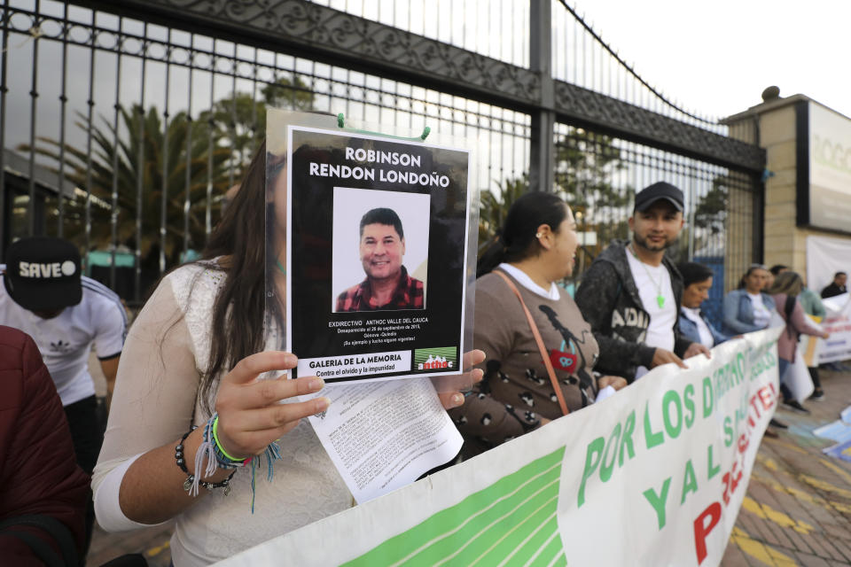 A woman holds a sign with a man's photo that say he disappeared in 2015, as she attends an anti-government protest outside the National Center for Historical Memory to call for the resignation of its director, Dario Acevedo, on Human Rights Day in Bogota, Colombia, Tuesday, Dec. 10, 2019. Protesters portray Acevedo as a henchman for the ruling conservative political party intent on masking the state’s role in crimes committed during the country’s long civil conflict. (AP Photo/Fernando Vergara)