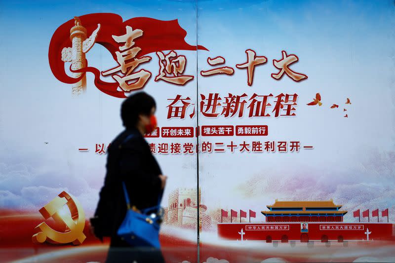 Woman walks past a poster welcoming the 20th National Congress of the Communist Party of China, in Beijing