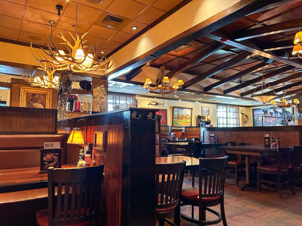 The interior of a LongHorn restaurant, with tables, chairs, paintings on the walls, and chandeliers with antlers.