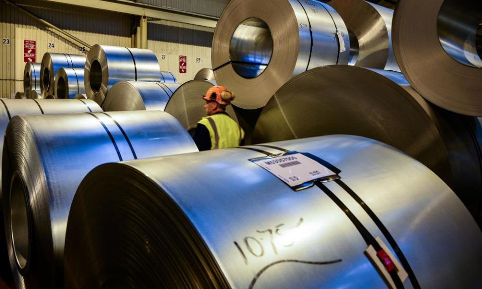 a factory worker walking past rolls of steel