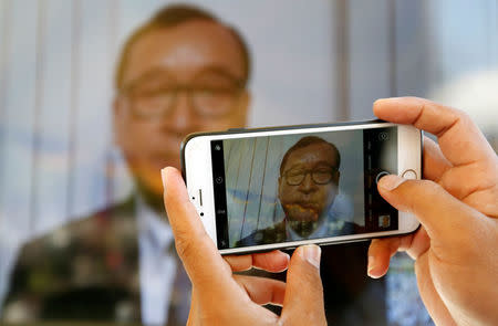 A man uses his smart phone to take picture from a television conference of Sam Rainsy, former President of the Cambodia National Rescue Party (CNRP), during a Buddhist ceremony for respecting at a statue commemorating the victims of a grenade attack on March 30, 1997, in Phnom Penh, Cambodia March 30, 2017. REUTERS/Samrang Pring