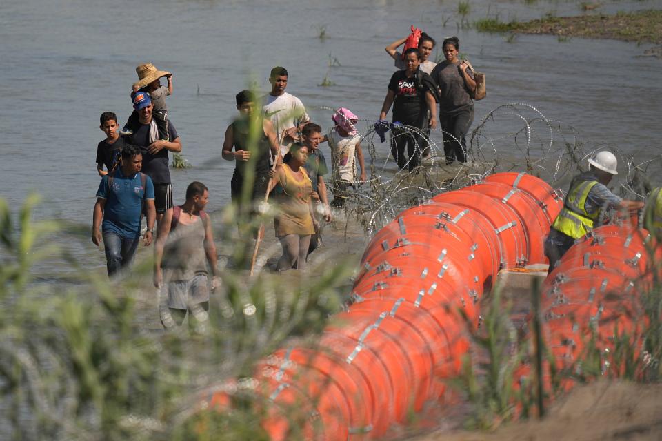 Migrants trying to enter the U.S. from Mexico on July 11 approach the site where workers are assembling large buoys to be used as a border barrier near Eagle Pass. The U.S. Justice Department is suing Texas over deploying the buoys in an international waterway without federal approval.