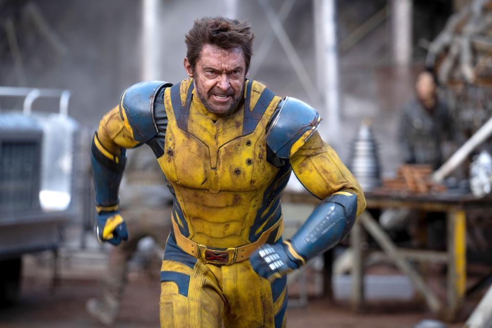 Hugh Jackman in a superhero costume, running with a determined expression in a rugged, industrial setting