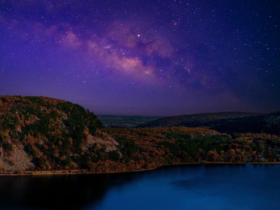 Stars begin to come out at twilight in Prineville Reservoir State Park.  The sky is a vibrant purple, streaked with pink fluffy views of the milky way. Below sits a sparsely shrubbed embankment.