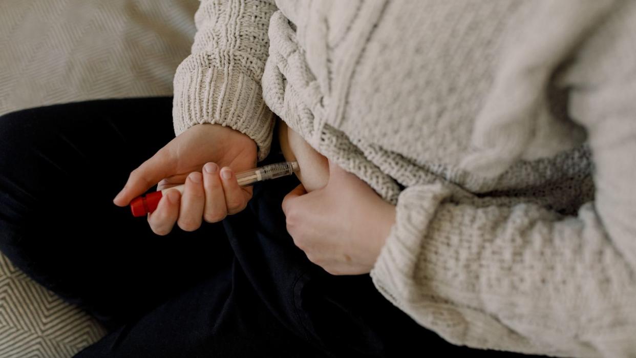 midsection of woman injecting syringe in abdomen during ivf test at home