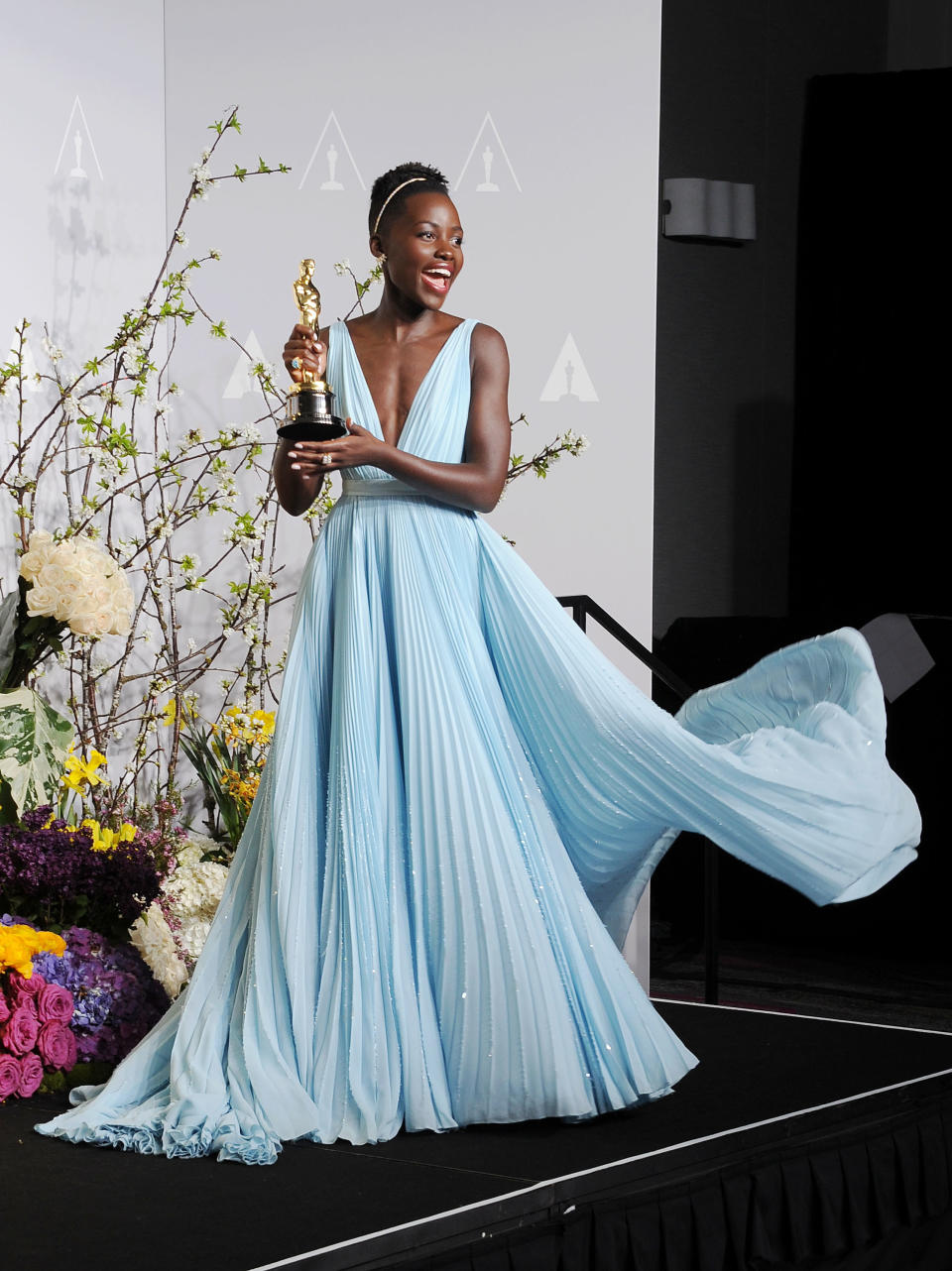 Lupita wearing a light blue elegant dress with a deep V-neck