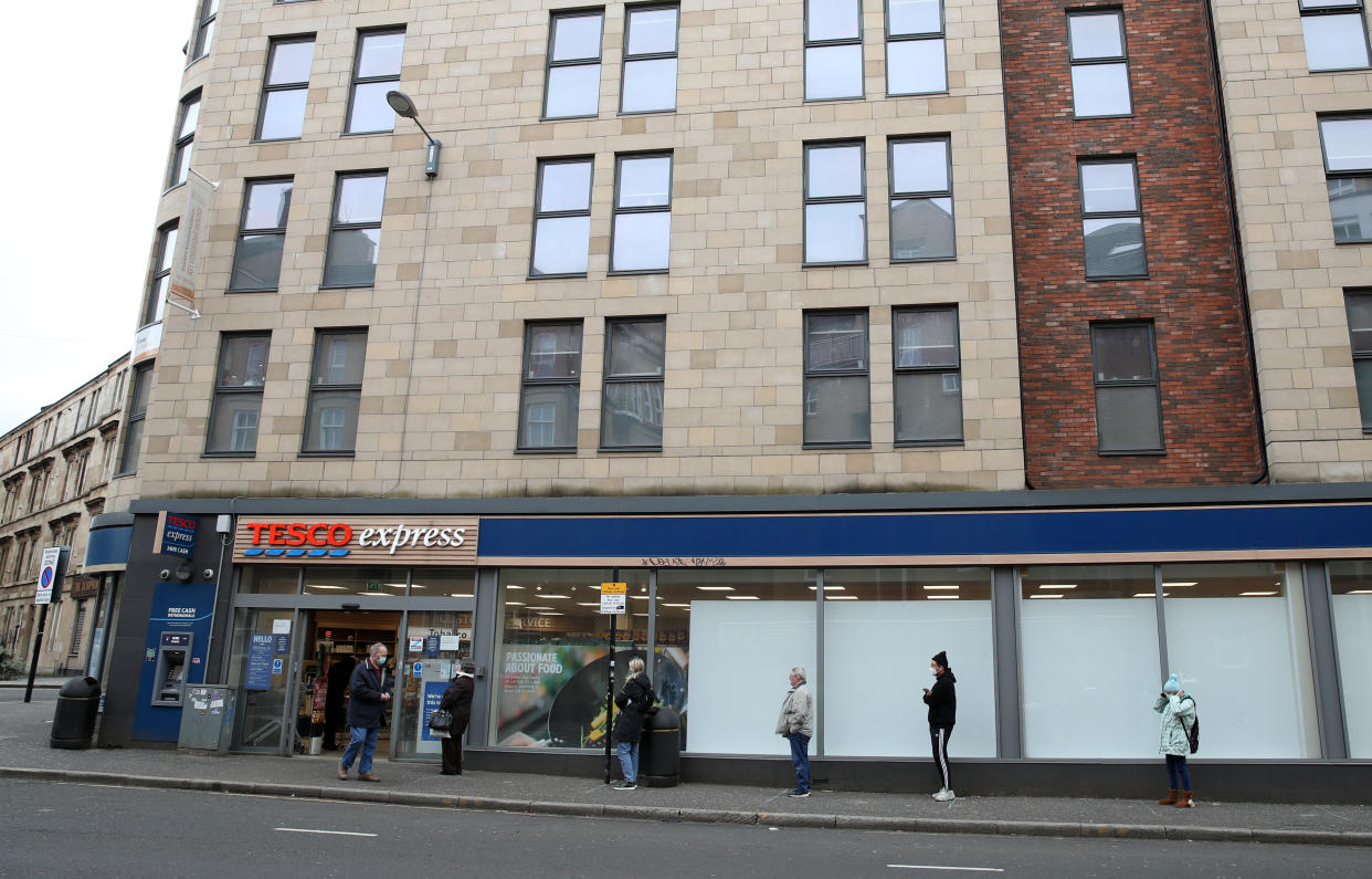 People follow social distancing guidelines as they queue outside a Tesco Express in Glasgow as the UK continues in lockdown to help curb the spread of the coronavirus.