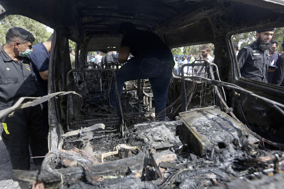 Pakistani investigators examine a burned van at the site of explosion in Karachi, Pakistan, Tuesday, April 26, 2022. The explosion ripped through a van inside a university campus in southern Pakistan on Tuesday, killing several people including Chinese nationals and their Pakistani driver, officials said. (AP Photo/Fareed Khan)