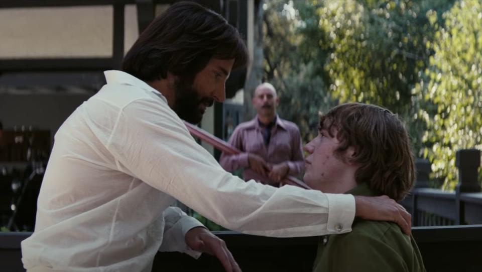 Bradley Cooper as Jon Peters puts his hand on a young man's shoulder in Licorice Pizza from Paul Thomas Anderson