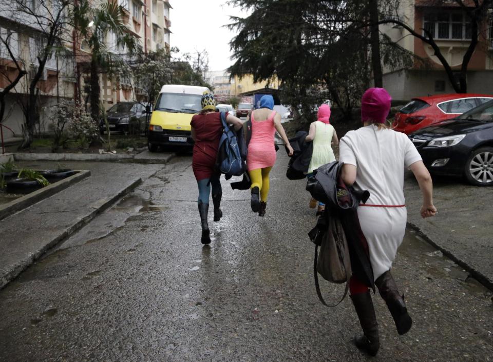 Russian punk group Pussy Riot members Nadezhda Tolokonnikova, in the blue balaclava, and Maria Alekhina, in the pink balaclava, run down the street with other women after they were released from a police station, Tuesday, Feb. 18, 2014, in Adler, Russia. No charges were filed against Tolokonnikova and Alekhina along with the others who were detained. (AP Photo/Morry Gash)