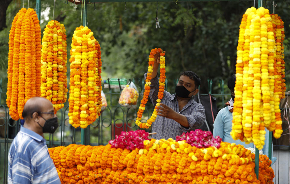 A roadside flower vendor covers his face with a mask and sells flowers outside a temple, in Prayagraj, India, Monday, June 8, 2020. Religious places, malls, hotels and restaurants open Monday after more than two months of lockdown as a precaution against coronavirus. (AP Photo/Rajesh Kumar Singh)