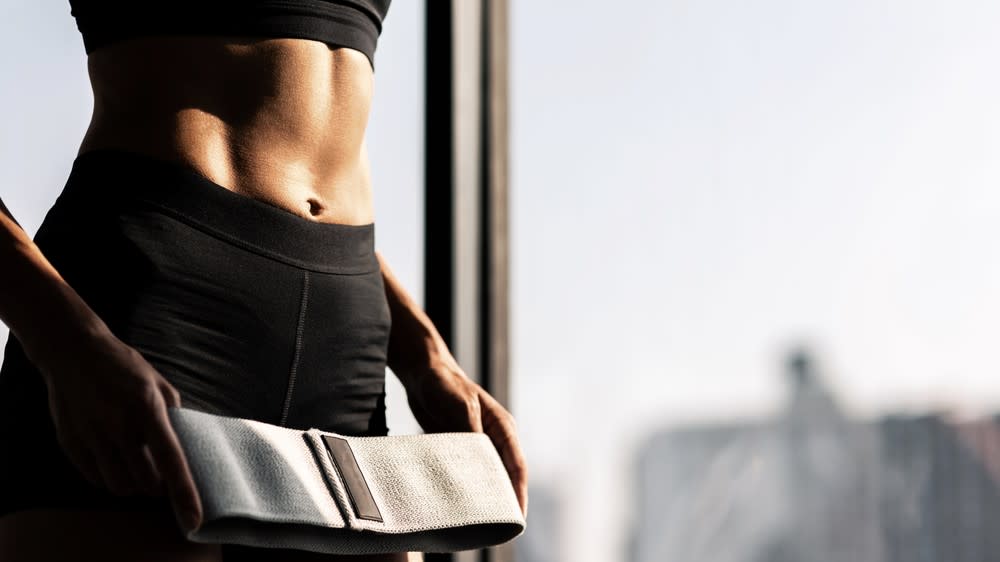  A photo of a woman with abs holding a resistance band. 