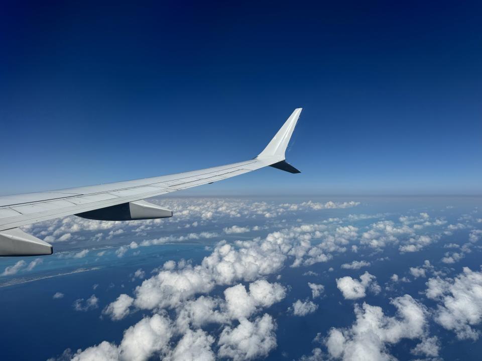 Airplane wing over clouds, seen from cabin window, set against a clear sky