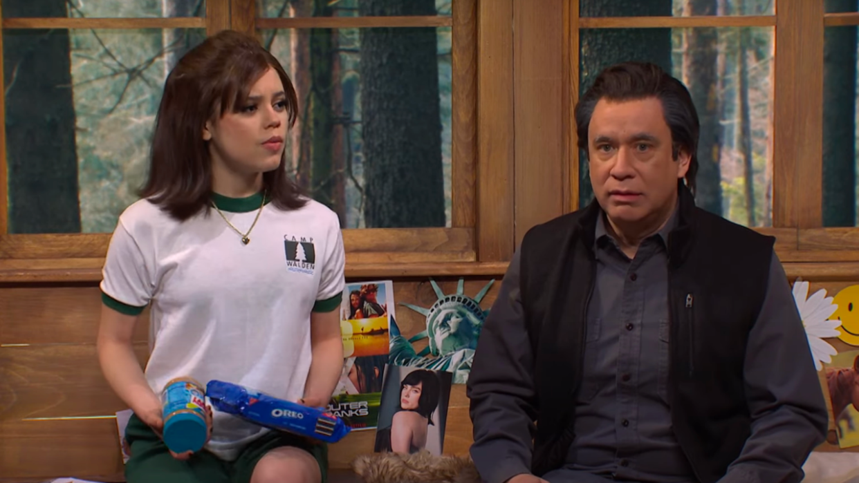  Fred Armisen and Jenna Ortega sitting on a bed and talking during an SNL sketch. 