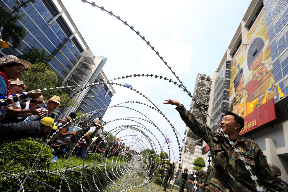 A Thai soldier tosses a bottle of drinking water over barbed wire, to anti-government protesters led by Suthep Thaugsuban, during a rally to disturb the work of Prime Minister Yingluck Shinawatra outside the office of Permanent Secretary for Defense, a temporary office of Yingluck on the outskirts of Bangkok, Thailand Wednesday, Feb. 19, 2014. Anti-government protesters surrounded Yingluck's temporary office in Bangkok's northern outskirts to demand her resignation a day after clashes with police. (AP Photo/Wason Wanichakorn)