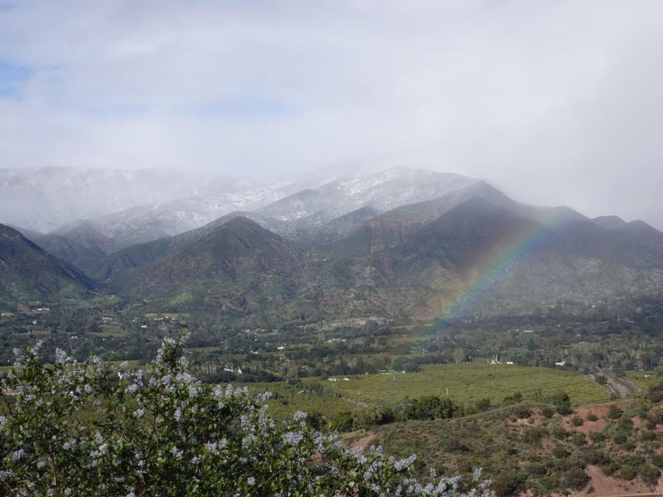 A rainbow, center right, arcs over the Ojai Valley as storm clouds move through the area, dusting mountains with snow, on Thursday.