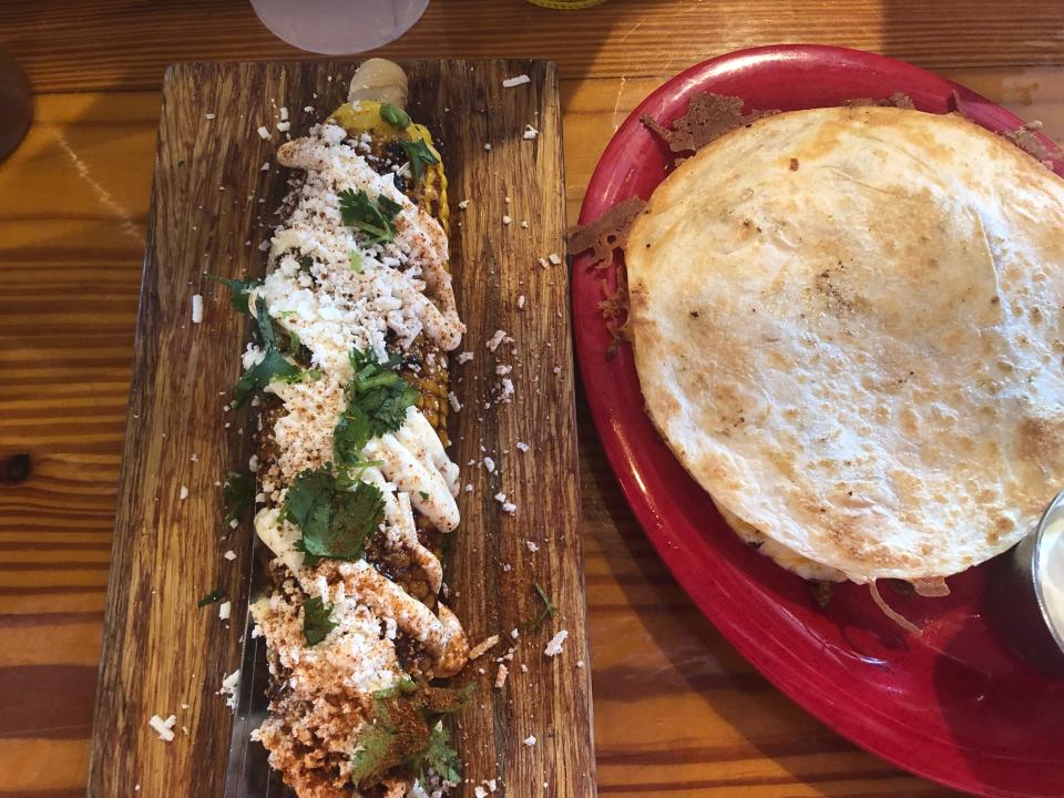 Elote, corn loaded with cheese and seasoning, next to a quesadilla on a plate