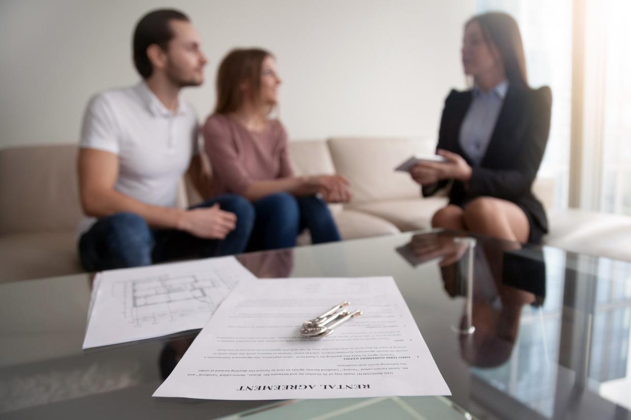 Couple talking to landlord about rent in background, focus on paper in foreground