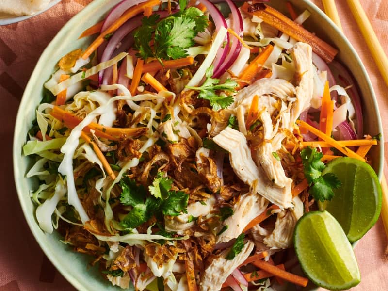 Vietnamese shredded chicken salad mixed with cabbage and carrots, garnished with fresh cilantro and lime; a pair of chopsticks and prawn chips are also on the table