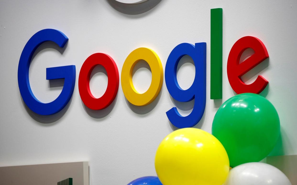 Coloured balloons float in front of a Google logo on a white wall