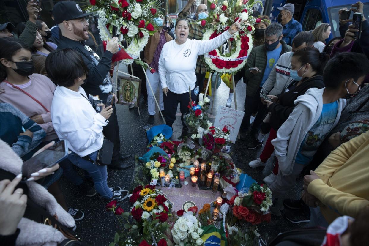 People gather around a memorial display of flowers