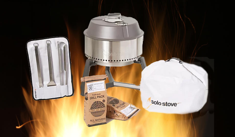 Silver Solo Stove grill on a stand with accompanying trio of grill tools, two grill packs and a white cover