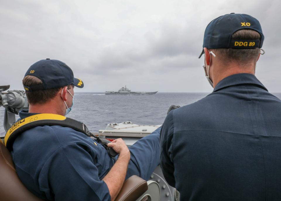 A US Navy commander and his colleague watch a Chinese aircraft carrier sail by.