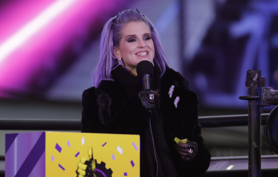 Kelly in a fur coat speaking into microphone on a podium