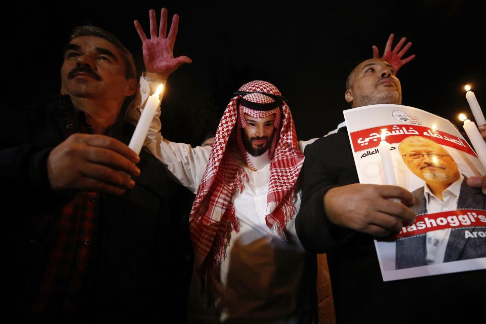 FILE- In this Oct. 25, 2018 file photo, an activist, wearing a mask depicting Saudi Crown Prince Mohammed bin Salman, holds up his hands, painted with fake blood as he protests the killing of Saudi journalist Jamal Khashoggi, during a candlelight vigil outside Saudi Arabia's consulate in Istanbul, Oct. 25, 2018. The poster in Arabic reads, "Khashoggi's Friends Around the World." The killing of Washington Post columnist Jamal Khashoggi at the Saudi Consulate in Istanbul drew renewed scrutiny to the kingdom, as his son and a U.N. investigator spoke out Tuesday, Oct. 1, 2019, ahead of the anniversary of his death. (AP Photo/Emrah Gurel, File)