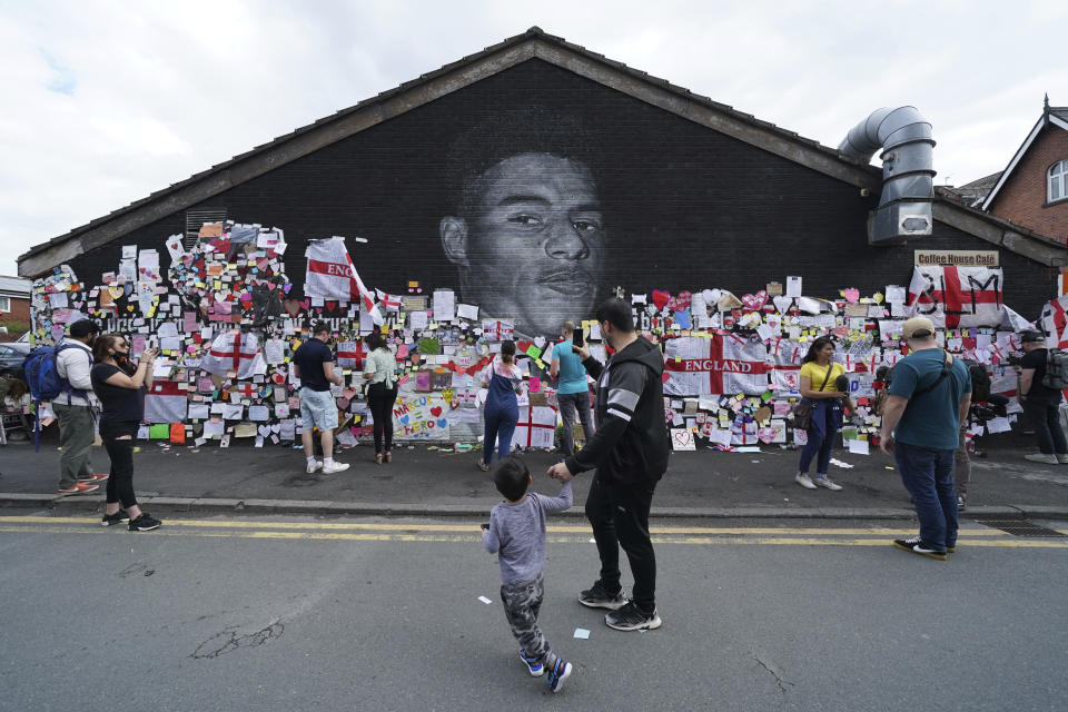 People look at the messages of support left on a mural of Manchester United striker and England player Marcus Rashford, on the wall of the Coffee House Cafe on Copson Street, in Withington, Manchester, England, Tuesday July 13, 2021. The mural was defaced with graffiti in the wake of England losing the Euro 2020 soccer championship final match to Italy. (AP Photo/Jon Super)