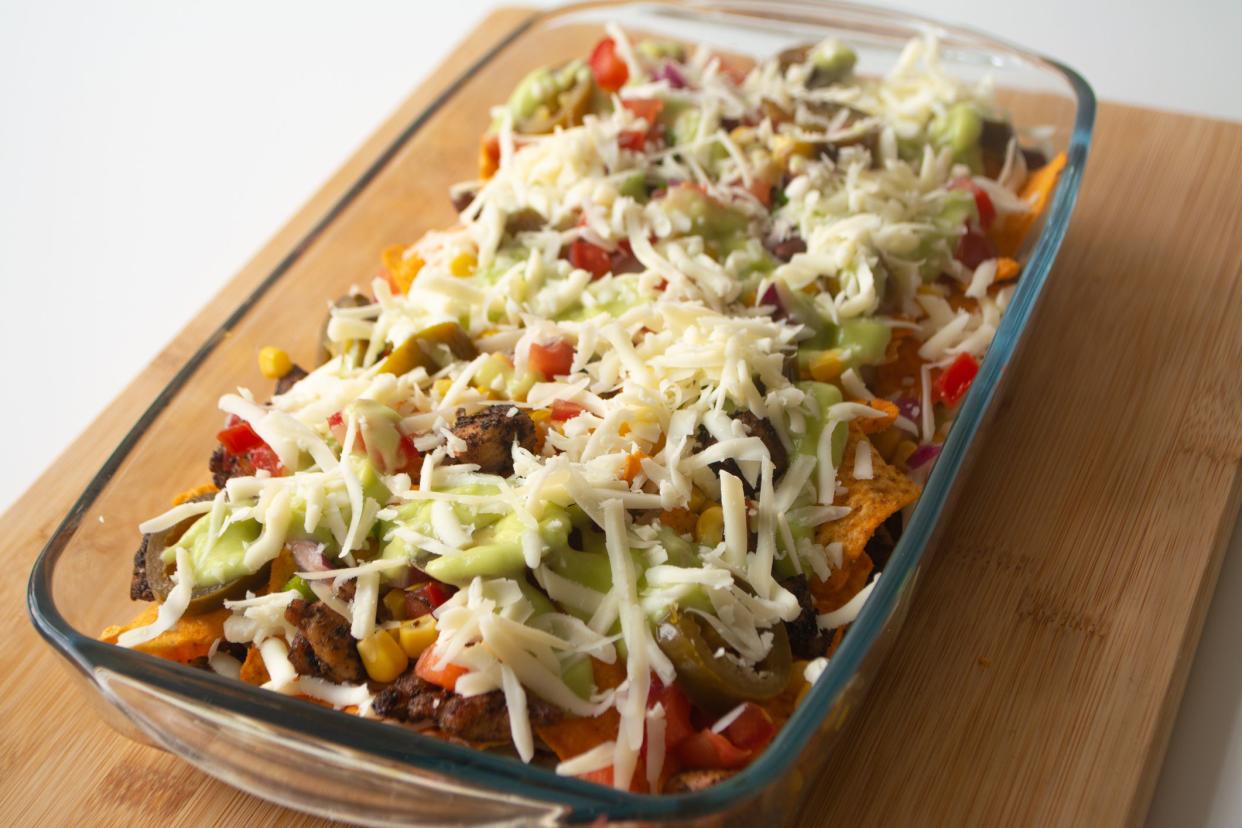 Baked nachos with corn tortilla chips, corn, guacamole, pico de gallo, beans, jalapenos and Monterrey jack in a glass baking dish