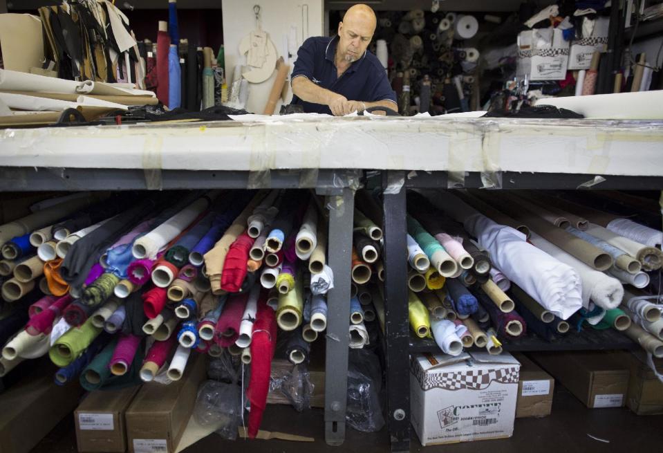 In this Aug 19, 2013 photo, fabric cutter Oscar Santa works on a table stacked with rolls of fabric in the New York studio of fashion designer Carmen Marc Valvo. Valvo will show his Spring 2014 show on Sept. 6 at Lincoln Center in New York. (AP Photo/John Minchillo)