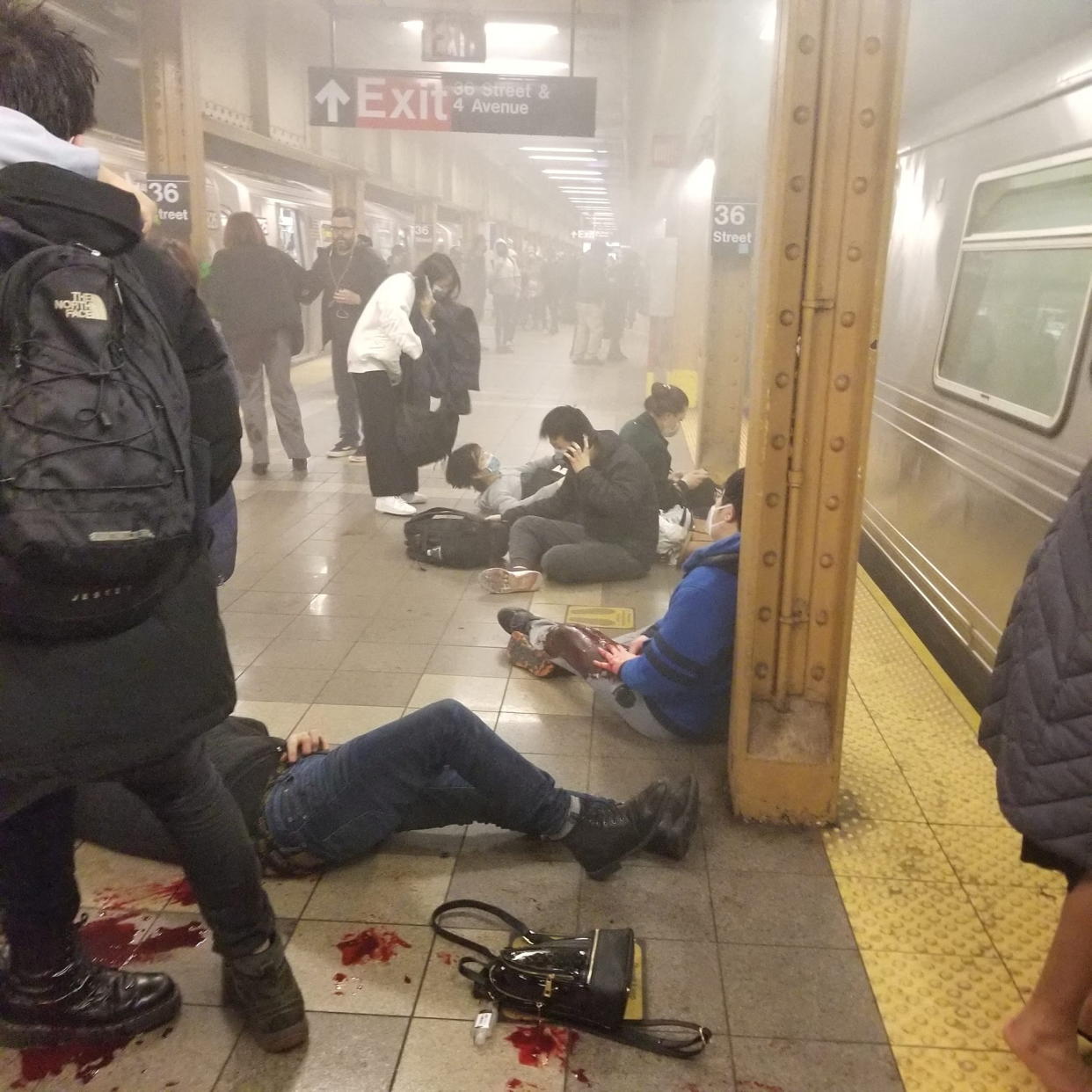 Wounded people stand, sit and lie on the platform at a smoke-filled subway station.