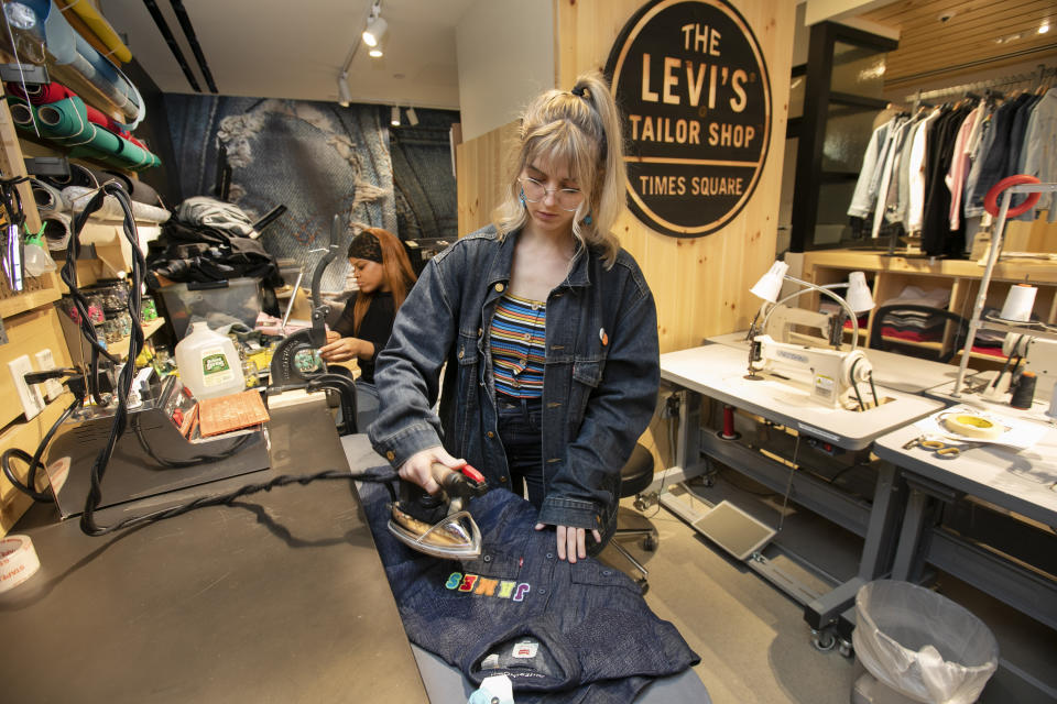 In this June 14, 2019, photo tailors Latoya Henderson, left, and Aly Reinert work in the Levi's Tailor Shop, in the Levi's store, in New York's Times Square. Levi Strauss & Co.’s new flagship in Manhattan’s Time Square features larger dressing rooms with call buttons and tailors who can add trims and patches to customers’ jeans. (AP Photo/Richard Drew)