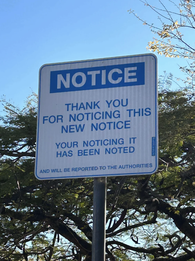 Sign reads: "NOTICE. Thank you for noticing this new notice. Your noticing it has been noted and will be reported to the authorities."