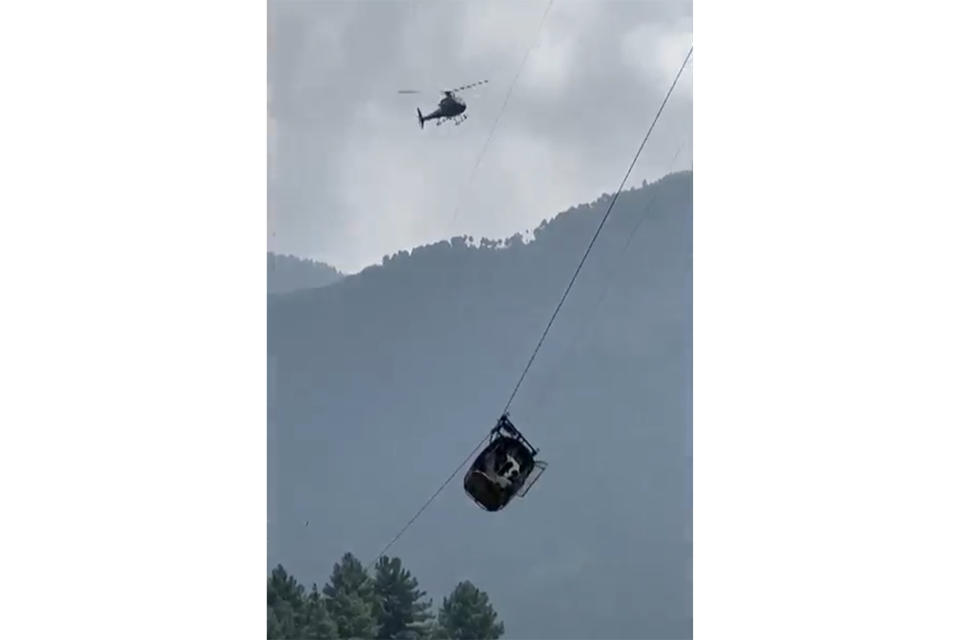 In this image taken from video, a cable car carrying six children and two adults dangles hundreds of meters (feet) above the ground in the remote Battagram district, Khyber Pakhtunkhwa, Pakistan on Tuesday, Aug. 22, 2023. The cable car malfunctioned, trapping the occupants for hours before rescuers arrived in helicopters to try to free them. (AP Photo)